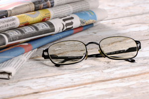 Glasses on top of a desk together with a bundle of newspaper.