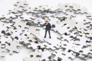 Businessman toy figure on the center of a broken puzzle pieces.