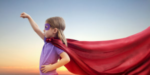 Kid wearing a mask and a cape playing as a superhero.